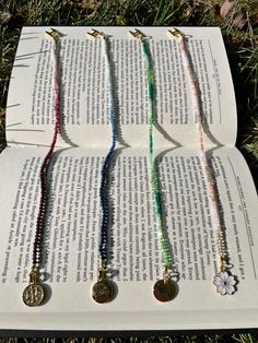 four necklaces are laying on top of an open book in the middle of some grass