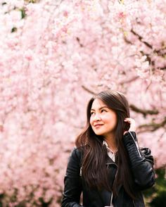 a woman standing in front of a tree with pink flowers