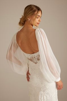 a woman in a white wedding dress with sheer sleeves on her back, looking at the camera