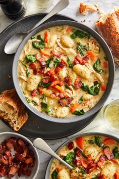 two bowls of pasta with spinach, bacon and cheese on the side next to bread