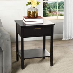 a black end table with flowers and books on it in front of a couch next to a window