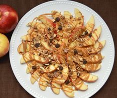 a white plate topped with sliced apples covered in caramel and chocolate chips next to an apple