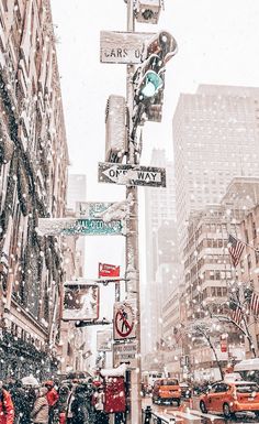 people are walking down the street in the snow with traffic lights and signs on poles