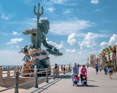 people walking on the boardwalk next to a statue