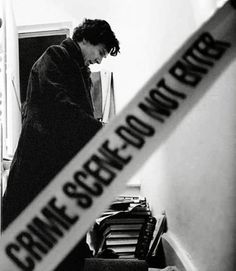 black and white photograph of a man standing next to a pile of books with a police tape on it