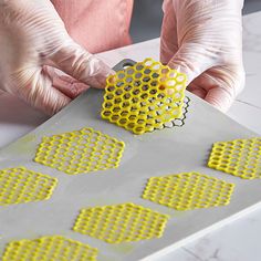 a person in white gloves is working on a piece of art with yellow circles and holes