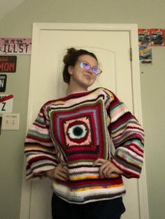 a woman standing in front of a door wearing a sweater with an eye patch on it