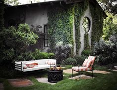 an outdoor living area with two chairs and a couch in front of a house covered in ivy