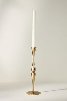 a gold candle holder with a single white candle in front of a plain wall background