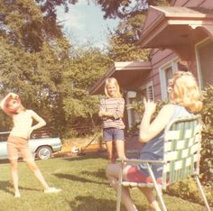 two girls are playing frisbee in the yard while another girl is watching them