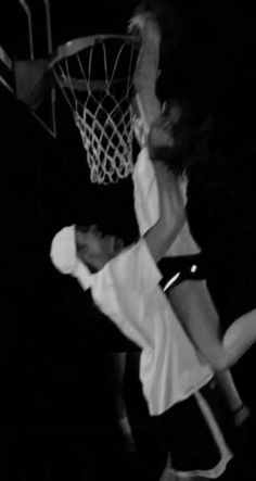 two people playing basketball in the dark with one person jumping up to dunk the ball