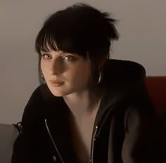 a woman with black hair and piercings sitting on a couch