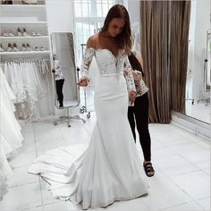 a woman standing in front of a mirror wearing a white wedding dress with long sleeves