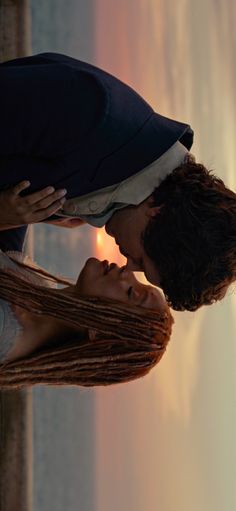 a man and woman kissing each other in front of a window with the sun setting behind them