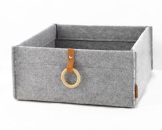 a gray felt storage box with a leather ring on the handle and handles, sitting on a white surface