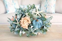 a vase filled with flowers and greenery on top of a wooden table next to a couch