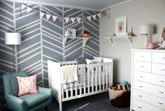 a baby's room with a white crib, blue chair and striped wallpaper