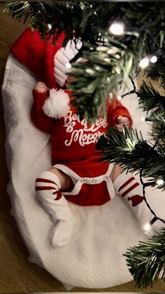 a baby in a red and white outfit laying under a christmas tree