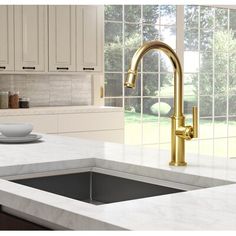 a modern kitchen with white cabinets and gold faucet, marble countertops, an island sink and large windows