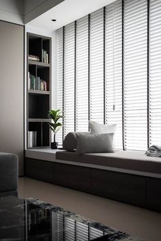 a living room filled with furniture next to a window covered in white blinds and bookshelves