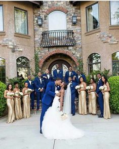 a bride and groom kissing in front of their wedding party at the entrance of a mansion