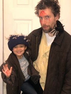 a man standing next to a little boy in front of a door with his face painted red