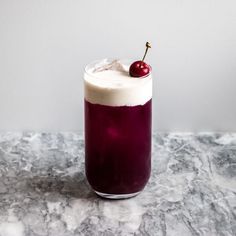 a purple drink with a cherry on the top and ice cream in it, sitting on a marble surface