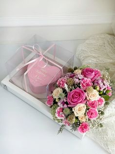 a bouquet of pink and white flowers sitting in a box next to a heart shaped box