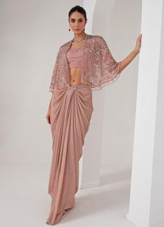 Elevate your style with the stunning Pastel Pink Draped Skirt with Embellished Cape, that effortlessly blends tradition with contemporary elegance. The pink cape features a sophisticated kimono sleeve , adorned with intricate florence embroidery using sequins, crystal tassels, cutdana, and bead highlights, adding a touch of opulence. Paired perfectly with a sequin jaal embellished blouse, it offers a dazzling appeal, making you the center of attention. Completed with a draped skirt, designed for a flattering silhouette, exudes grace and charm, ensuring comfort and sophistication in every movement. Ideal for, this ensemble is a timeless addition to your wardrobe, exuding both modernity and tradition in every detail. Composition : Cape - Organza ,Skirt - Platinoir Crepe Care: Dry Clean Only Cape Outfit, Drape Sarees, Embroidered Cape, Pink Cape, Saree Tassels, Pink Kimono, Indian Wedding Wear, Draped Skirt, Embellished Blouse