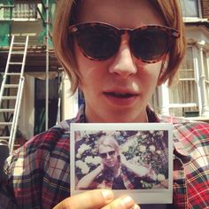 a woman wearing sunglasses holding up a polaroid photo