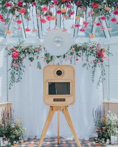 a wooden tripod with flowers hanging from it's sides and a camera on top