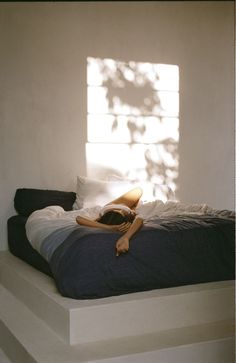 a woman laying on top of a bed in a room with sunlight coming through the window