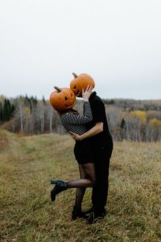 a man and woman hugging each other with pumpkins on their heads in an open field