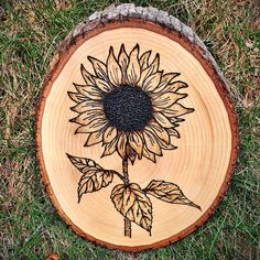 a sunflower painted on a piece of wood sitting in the middle of some grass