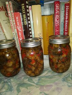 three jars filled with pickled vegetables on top of a table next to bookshelves