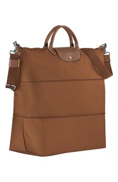 A zip inset expands and contracts a durable, water-resistant nylon travel bag trimmed with rich brown leather. Top zip closure. Removable crossbody strap. Interior wall pocket. Water-resistant lining. Folds flat for storage. Nylon with leather trim. By Longchamp; imported. Handbags. Longchamp Travel Bag, Brown Travel Bag With Turn-lock Closure, Brown Leather Trim Travel Bag For On-the-go, Longchamp Le Pliage Pouch With Handle, Longchamp Expandable Travel Bag, Brown Leather Top, Nylon Travel Bag, Wall Pockets, Interior Wall