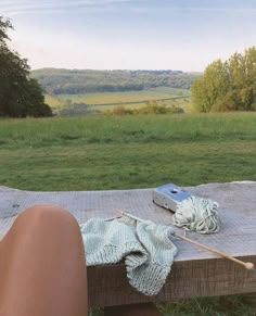 a person's feet resting on a picnic table with a book and knitting needle