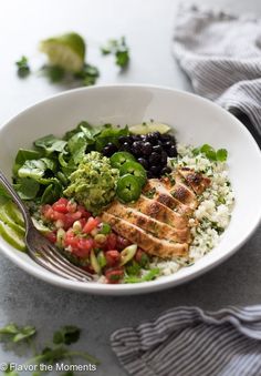 a white bowl filled with rice, black beans and avocado next to a fork