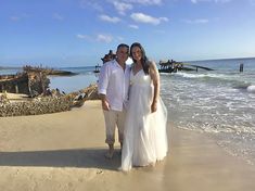 a man and woman standing on top of a sandy beach next to the ocean,