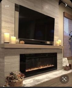 a living room with a fireplace and television mounted on the wall above it is lit by candles