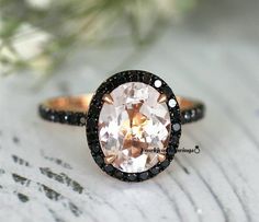 a ring with an oval shaped morganite surrounded by black and white diamonds