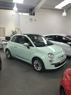 a light blue car is parked in a showroom next to other cars on the floor