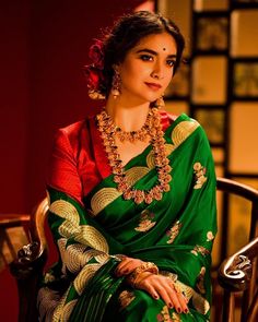 a woman in a green sari sitting on a chair and smiling at the camera