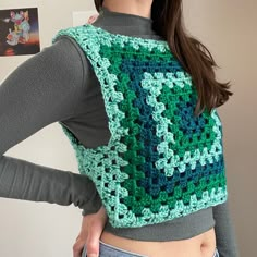 a woman wearing a green and blue crochet granny square sweater with her back turned to the camera