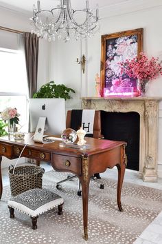 a desk with a laptop on it in front of a fire place and chandelier