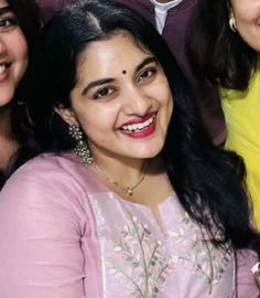 three women are smiling and posing for a photo together, one is wearing a pink dress