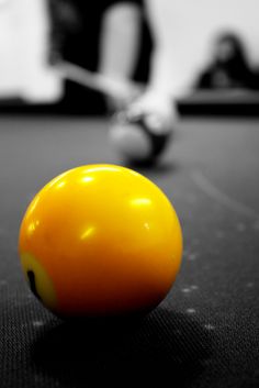 a yellow ball sitting on top of a pool table next to two people in the background