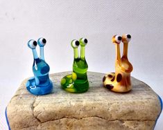 three glass snails sitting on top of a rock