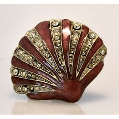 a red and gold shell shaped brooch with crystal stones on the bottom, sitting on a white surface