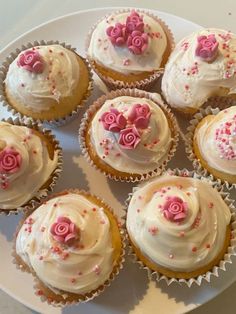 twelve cupcakes with white frosting and pink roses on top are sitting on a plate